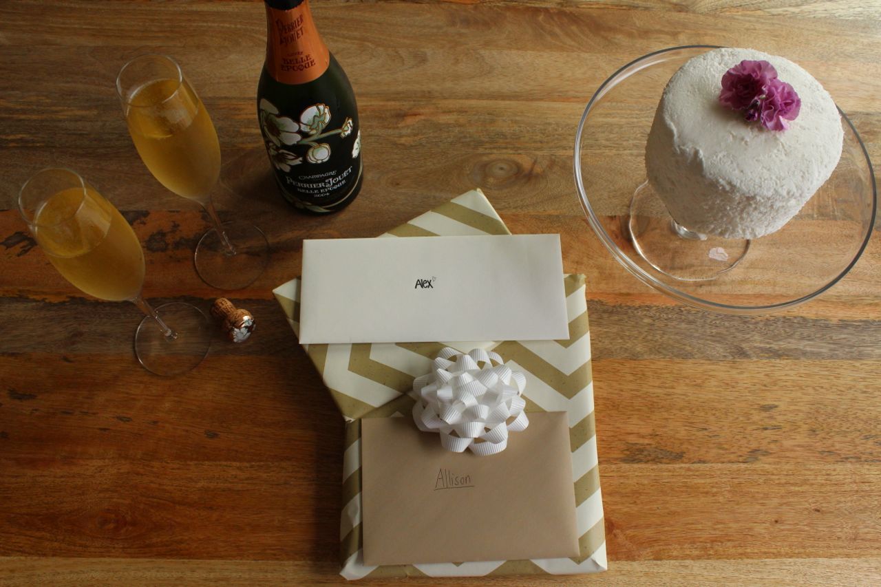 the top tier of a wedding cake on a wooden table with champagne and anniversary gifts