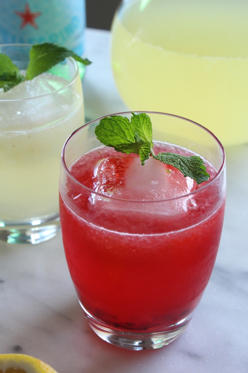 red drink in a glass with a large ice cube and a sprig of fresh mint
