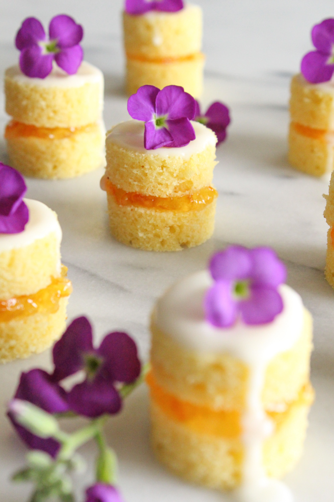 side view of mini naked cakes layered with orange marmalade and topped with vanilla glaze a tiny purple flower