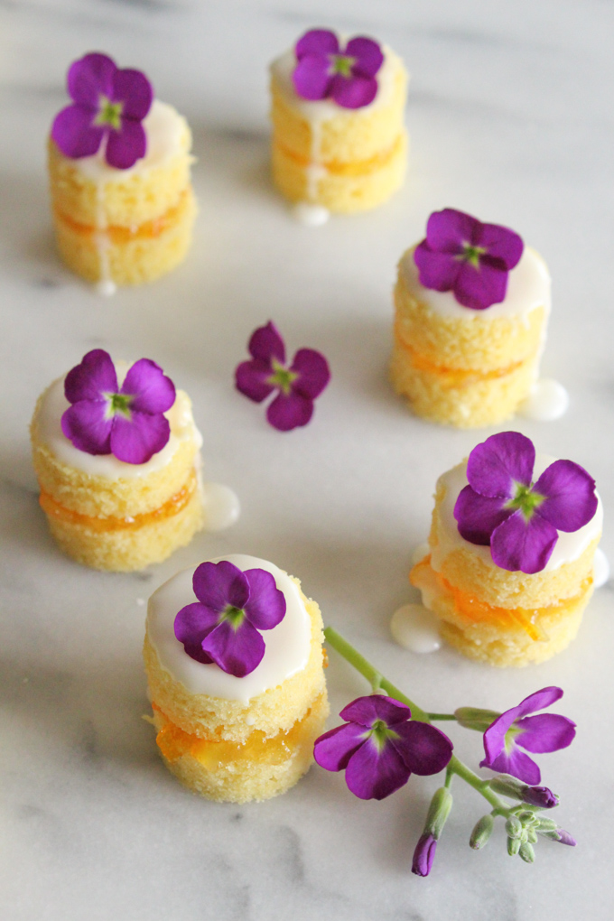 angled view of mini naked cakes topped with vanilla glaze a tiny purple flower