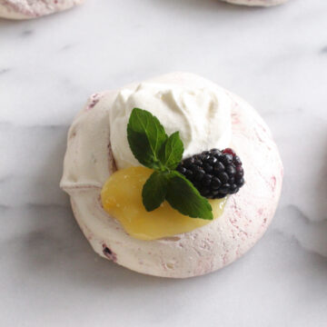 overhead view of meringue topped with lemon curd, whipped cream, blackberry, and mint sprig on a marble surface