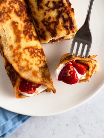 close up view of rolled crepe pancakes with fresh strawberries on a white plate