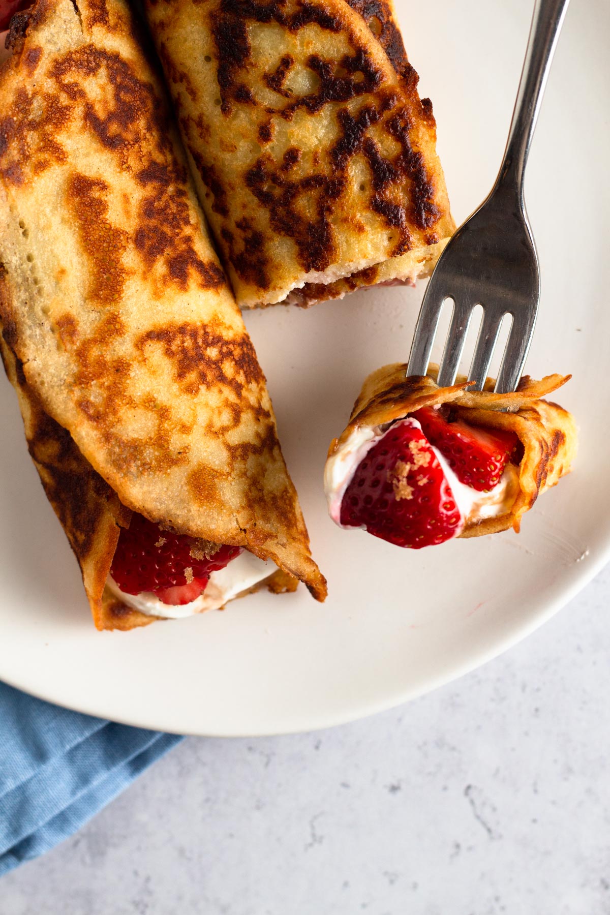 close up view of rolled crepe pancakes with fresh strawberries on a white plate