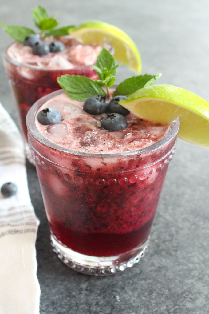 Mocktail in a glass garnished with fresh blueberries, mint, and a lime wedge.