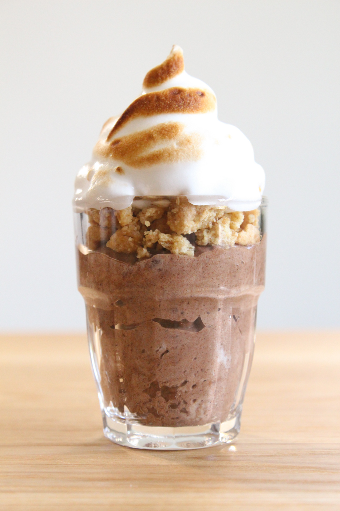 shot glass layered with chocolate mousse, graham cracker crumbles, and marshmallow topping on a wooden surface