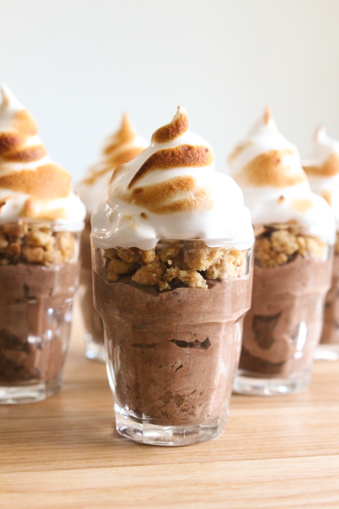 shot glasses layered with chocolate mousse, graham cracker crumbles, and marshmallow topping on a wooden surface