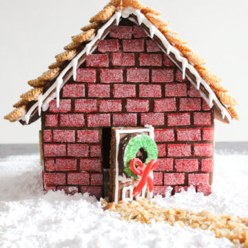 Gingerbread house with red "brick" walls on a powdered sugar-covered surface.