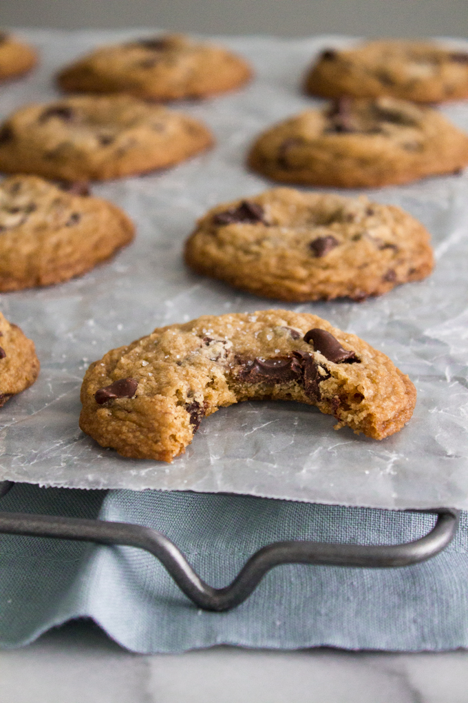 angled view of a chewy chocolate chip cookie with a bite missing on a wax paper-lined cooling rack