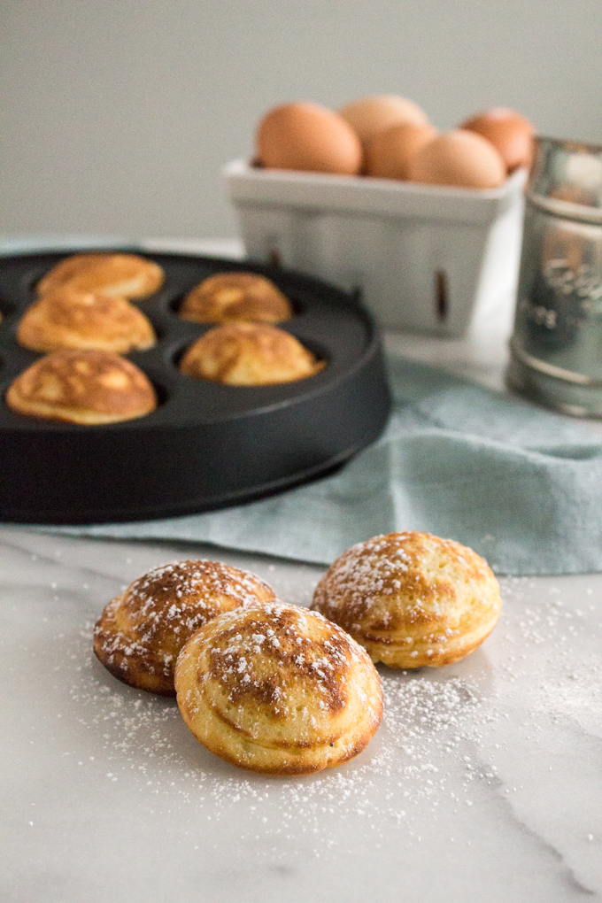 side view of Nutella-stuffed ebelskivers (Danish pancakes) dusted with confectioners' sugar on a marble surface