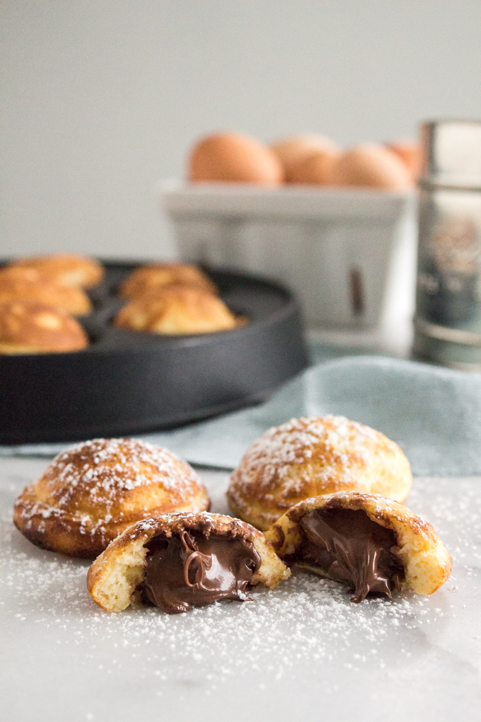 side view of Nutella-stuffed ebelskivers (Danish pancakes) dusted with confectioners' sugar on a marble surface