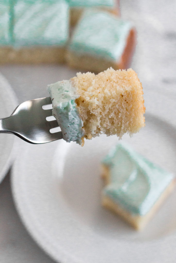 Forkful of vanilla cake with light blue frosting.