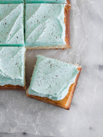Square cake slices topped with speckled frosting on a marble surface.