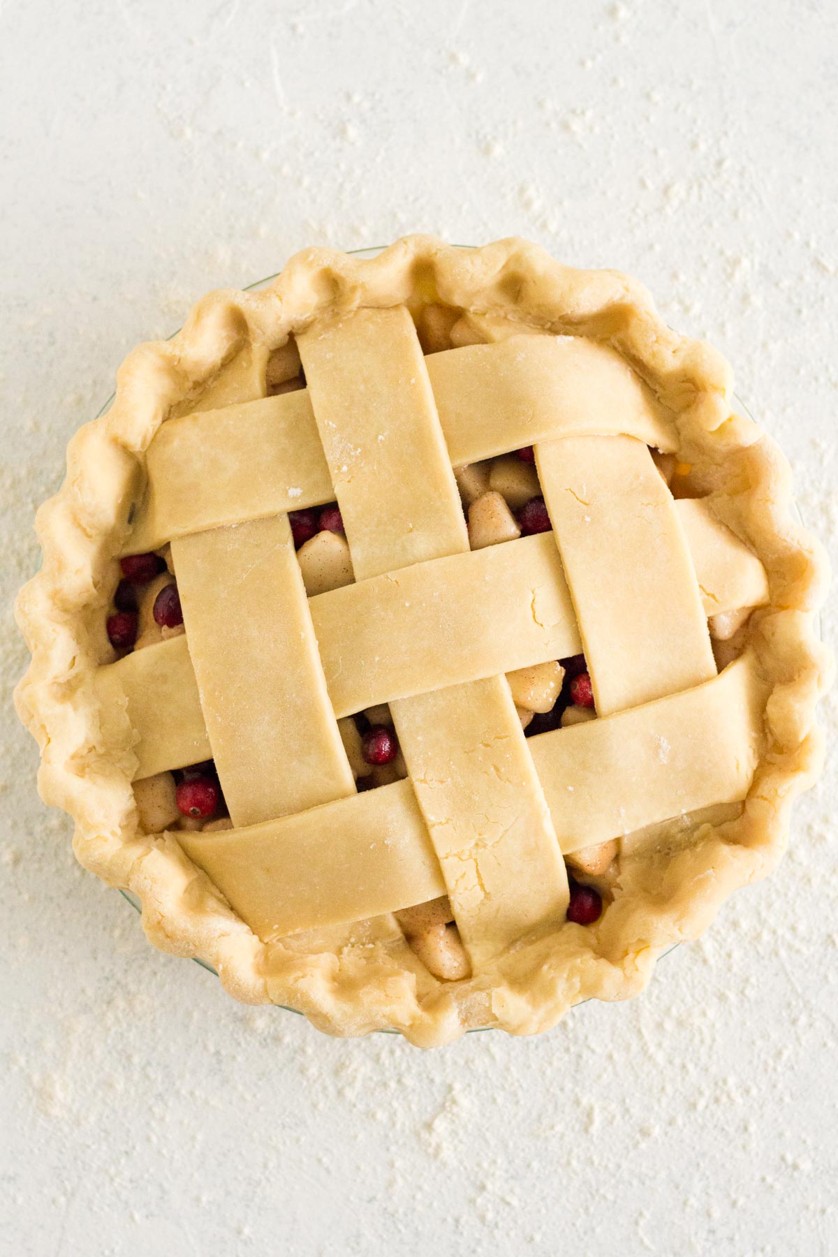 Overhead view of unbaked pie with lattice top on a white surface.