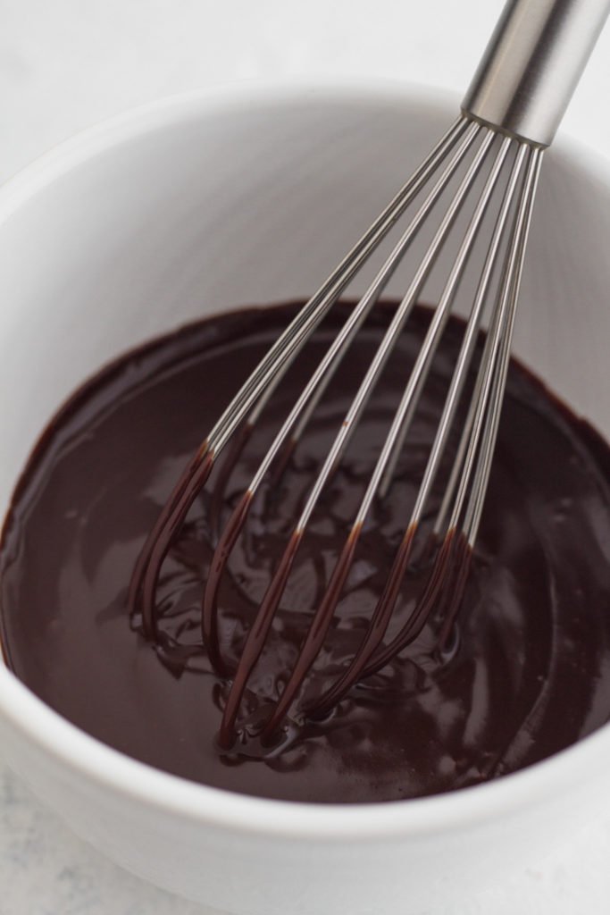 close up overhead view of chocolate ganache in a white bowl with a metal whisk