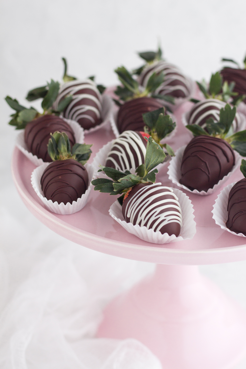 Angled view of chocolate covered strawberries on a pink cake stand.