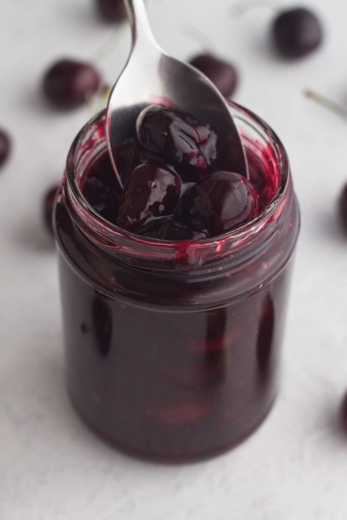 angled view of homemade cherry sauce in a glass jar with a spoon scooping the sauce