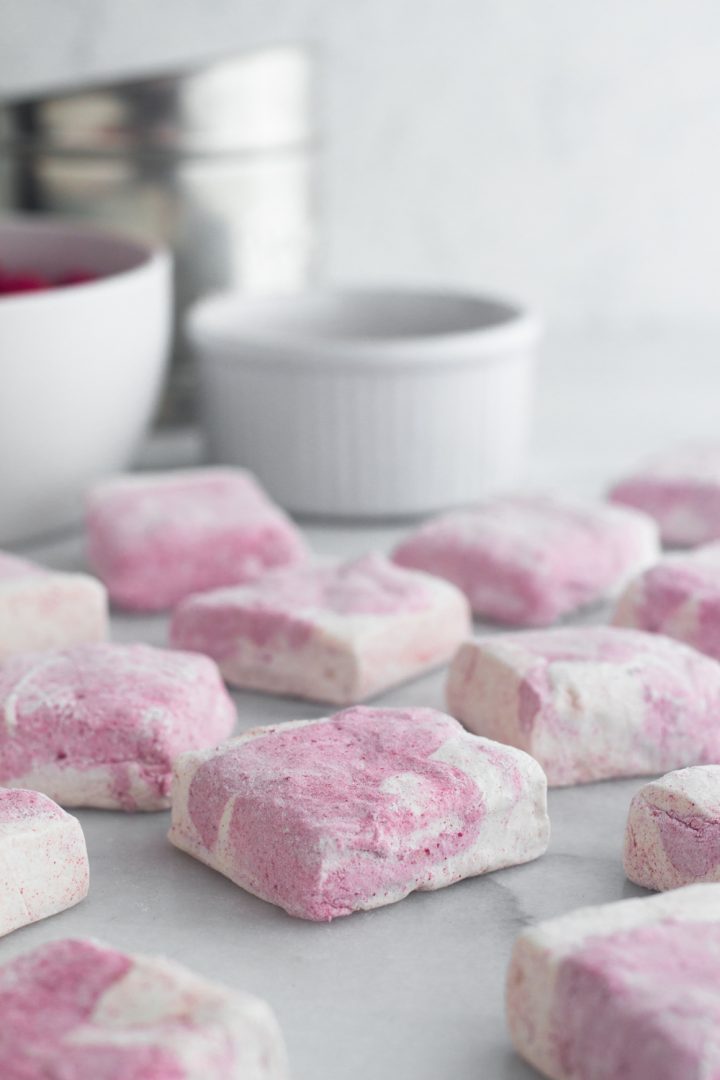 angled view of homemade raspberry swirl marshmallows on a marble surface