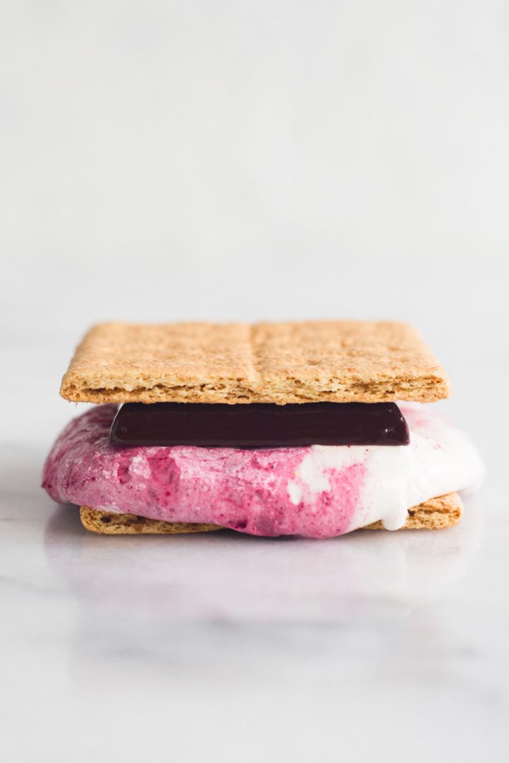 side view of a s'more made with homemade raspberry swirl marshmallows and dark chocolate on a marble surface