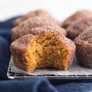 side view of a bitten pumpkin spice donut muffin on a cooling rack with a navy blue linen napkin