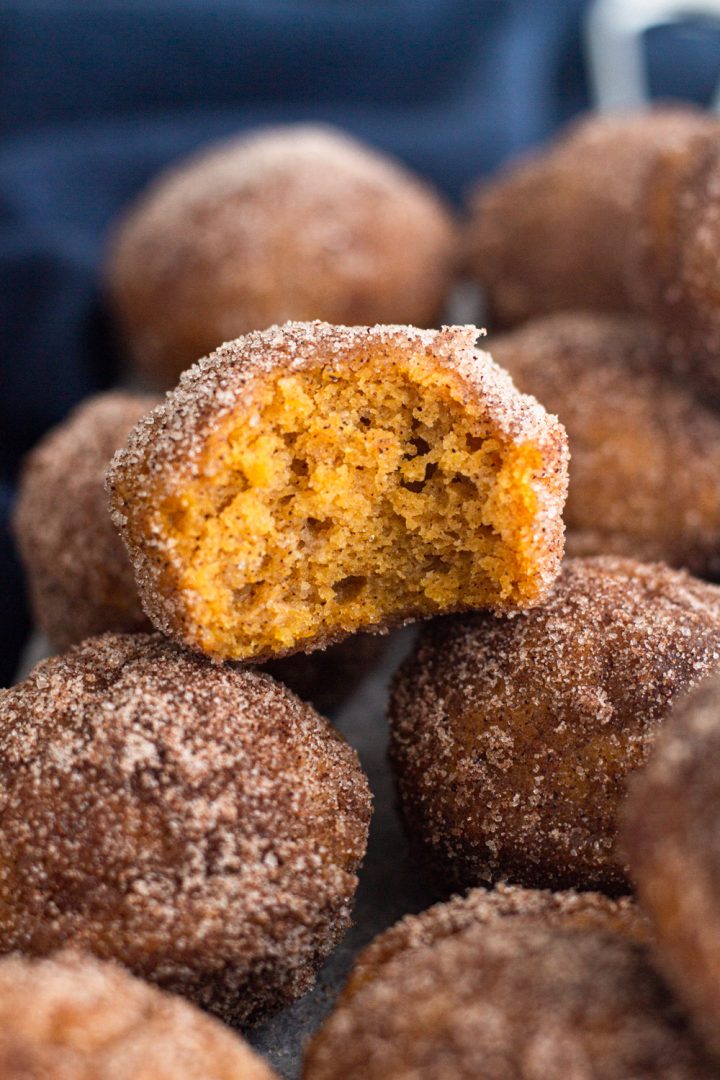 angled view of a bitten mini pumpkin spice donut muffin stacked on top of other mini donut muffins with a navy blue linen napkin