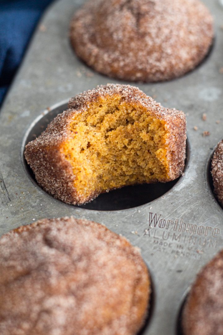 angled view of a bitten pumpkin spice donut muffin in a muffin tin