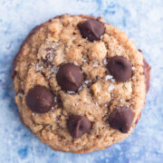 close up overhead view of a whole wheat chocolate chip cookie sprinkled with sea salt on a blue surface