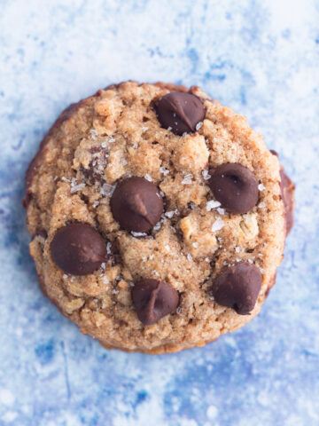 close up overhead view of a whole wheat chocolate chip cookie sprinkled with sea salt on a blue surface