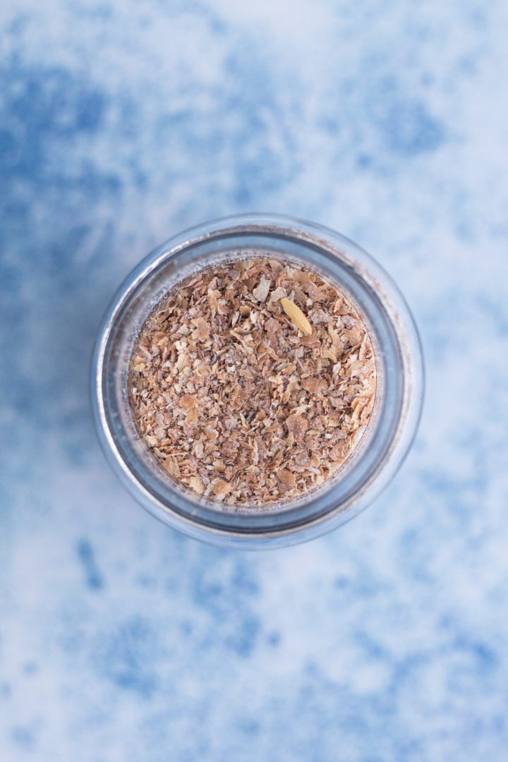 overhead view of wheat bran in a glass jar on a blue surface
