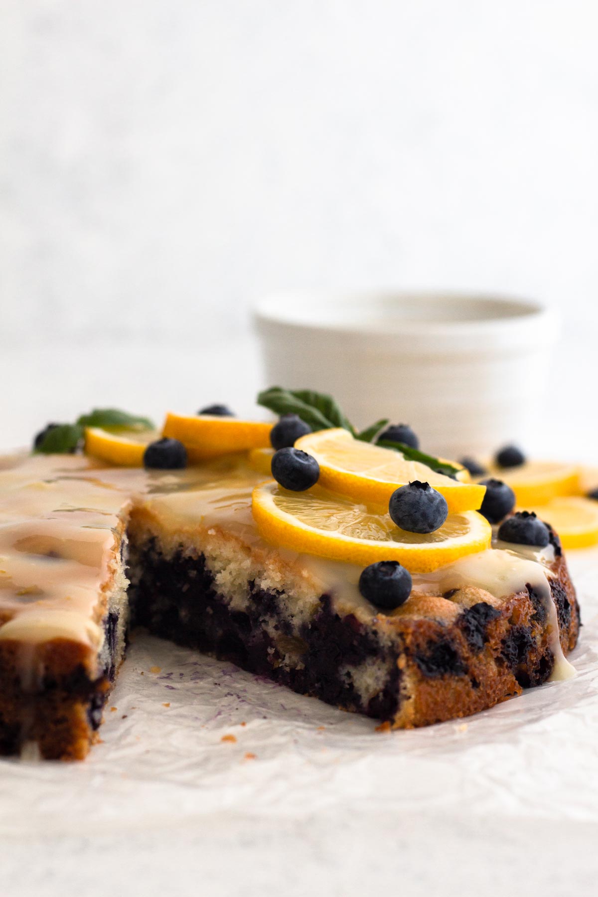 Side view of sliced blueberry cake topped with fresh blueberries and lemon slices.