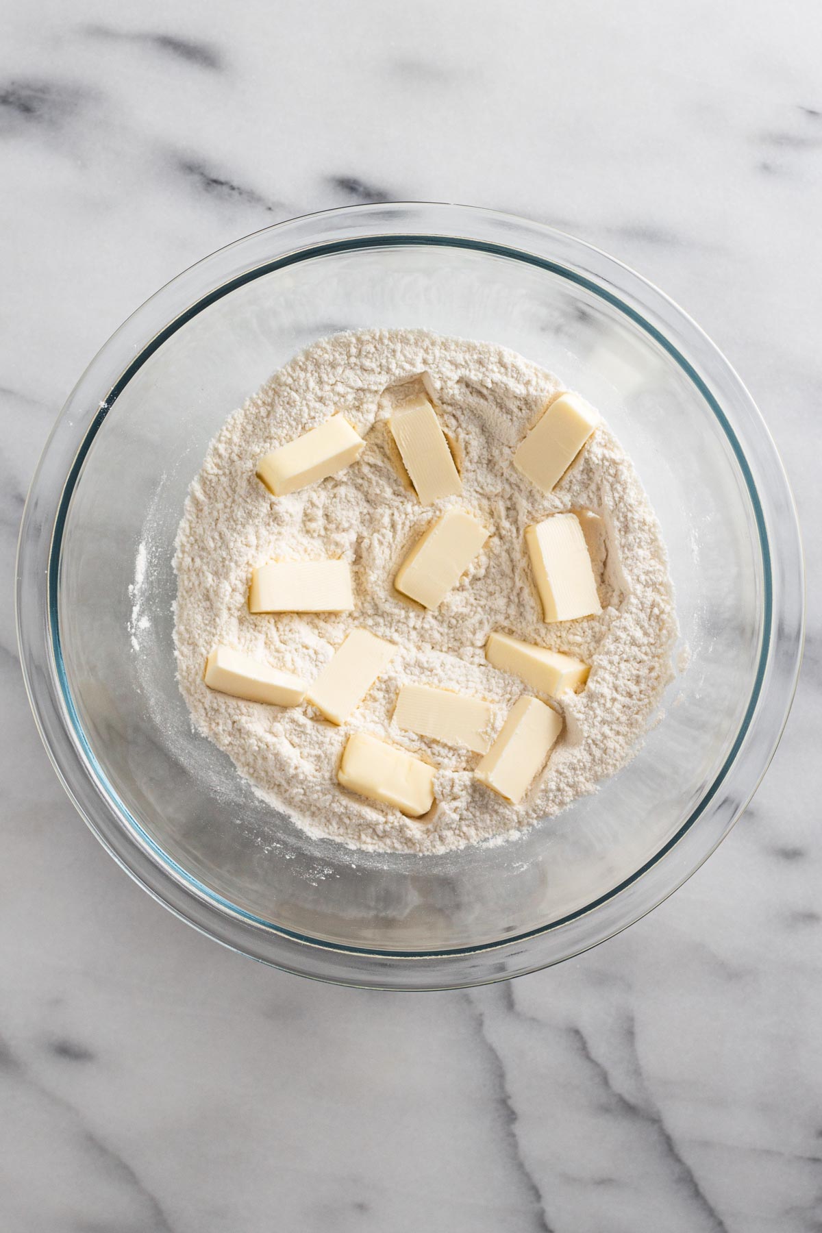 overhead view of dry ingredients in a glass bowl with cubed butter