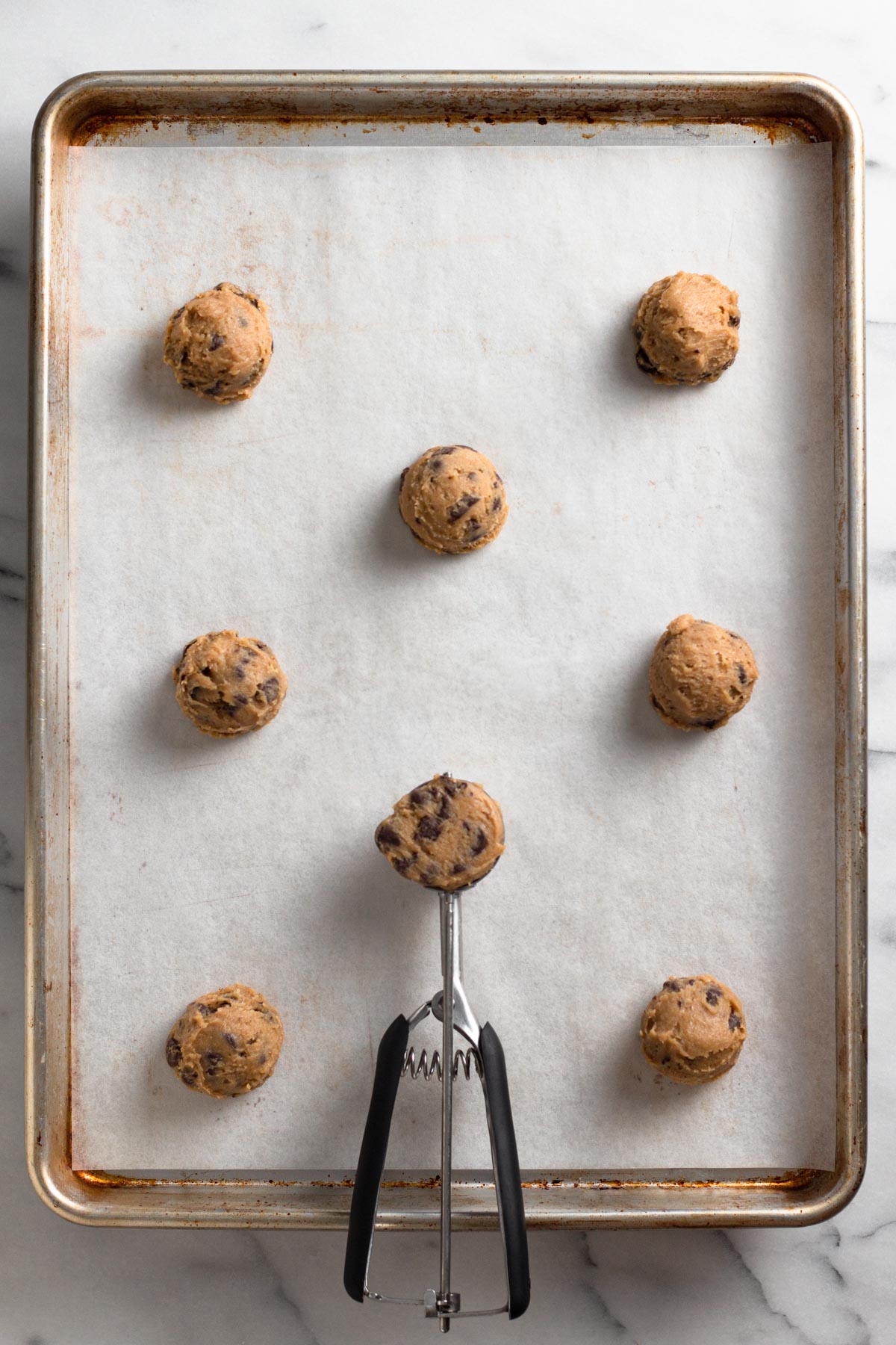 overhead view of cookie dough balls and a cookie scoop on a baking sheet