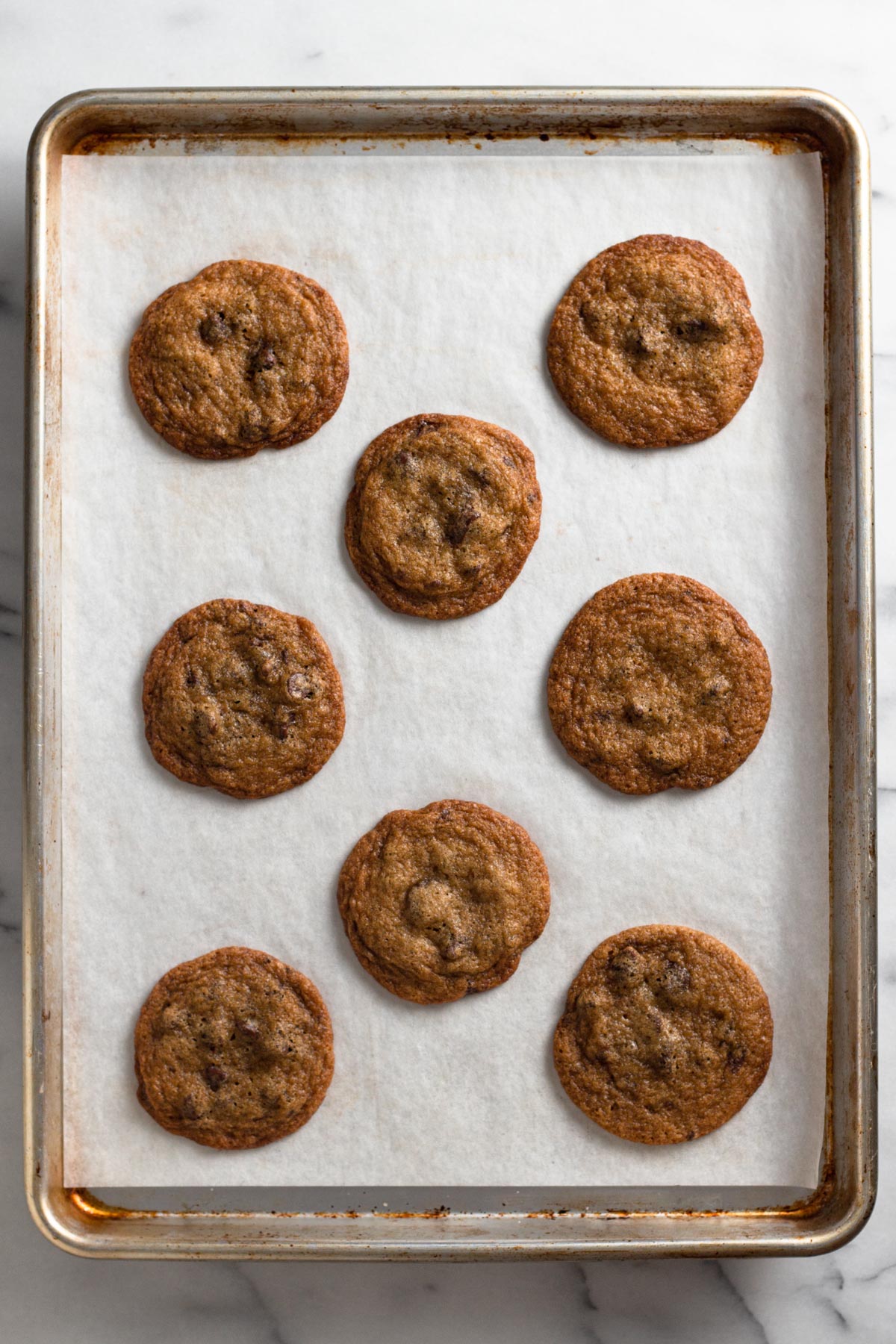 overhead view of perfectly round baked chocolate chip cookies on a baking sheet