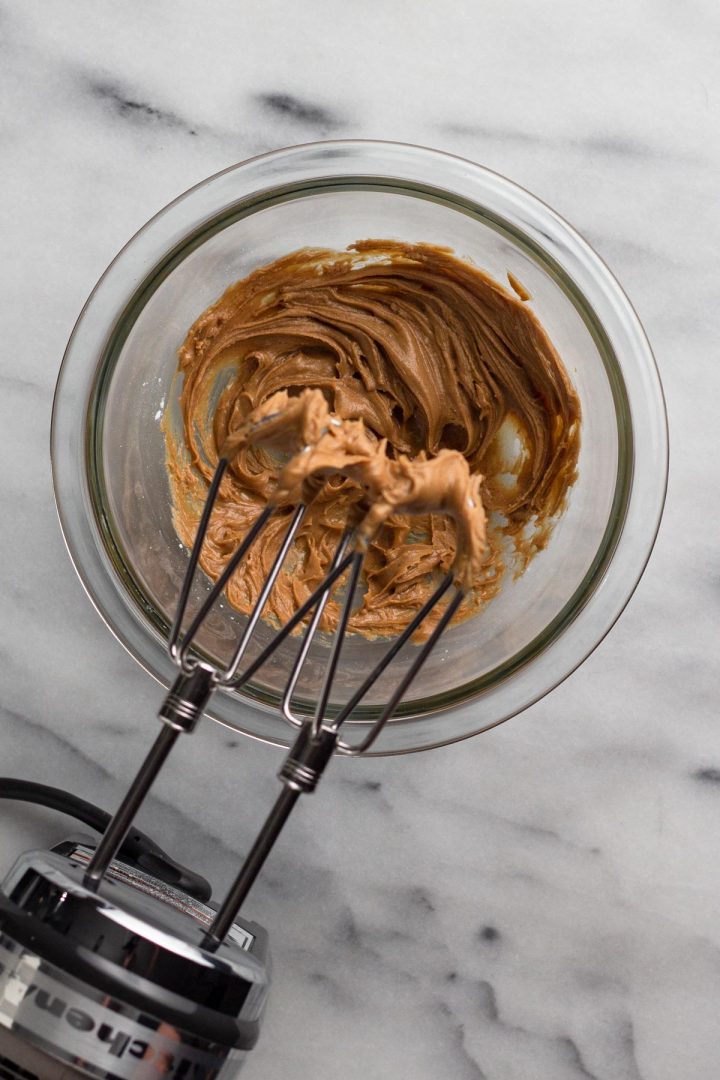 overhead view of peanut butter filling in a glass bowl with a hand mixer