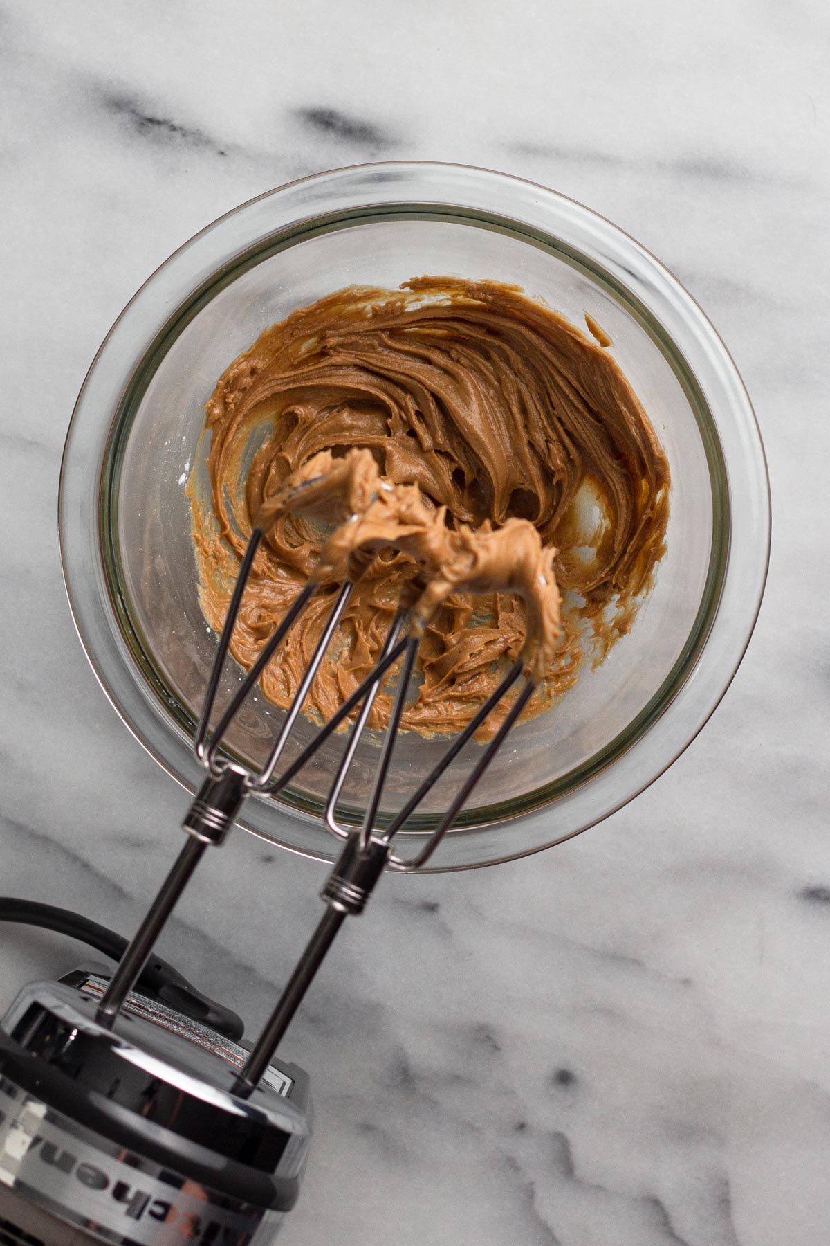 Overhead view of peanut butter filling in a glass bowl with a hand mixer.