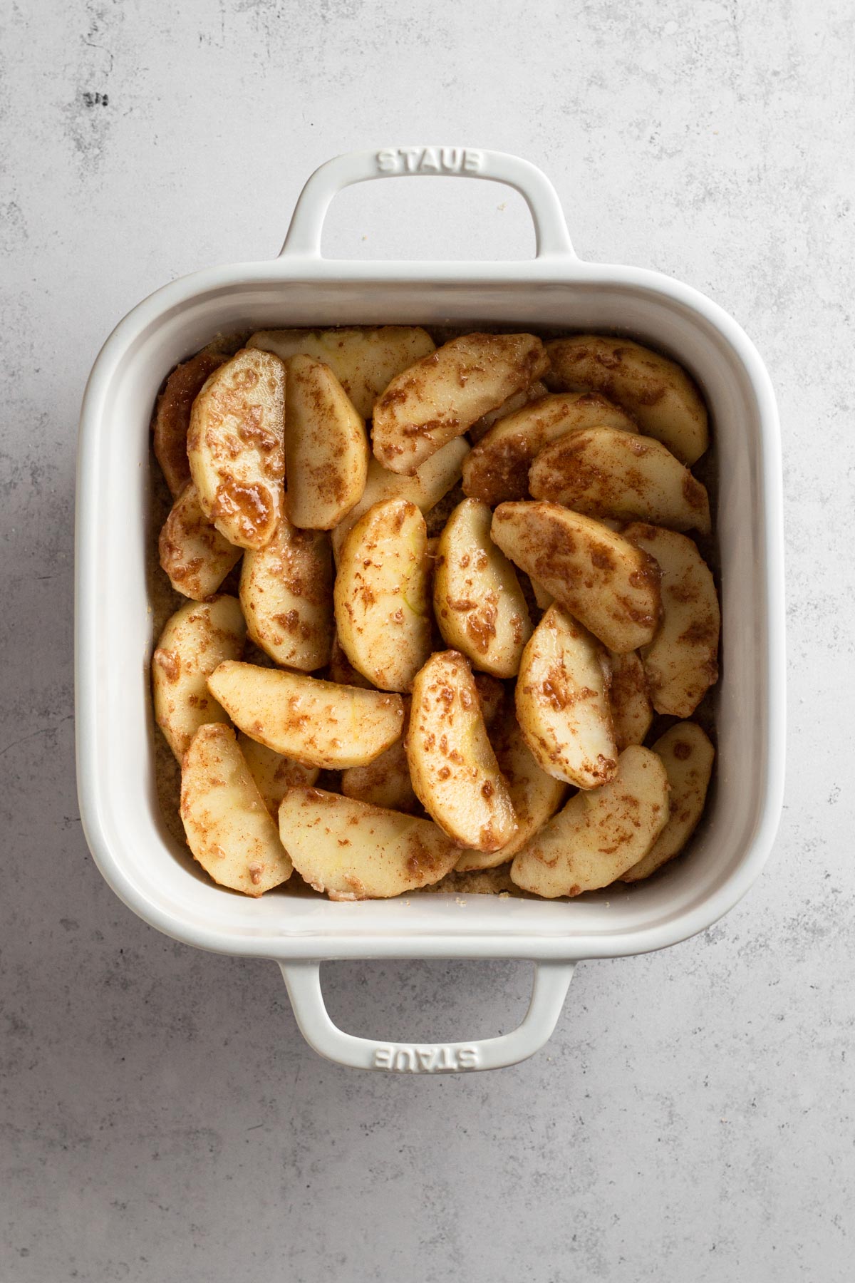 Seasoned apple slices atop shortbread crust in a white baking dish.