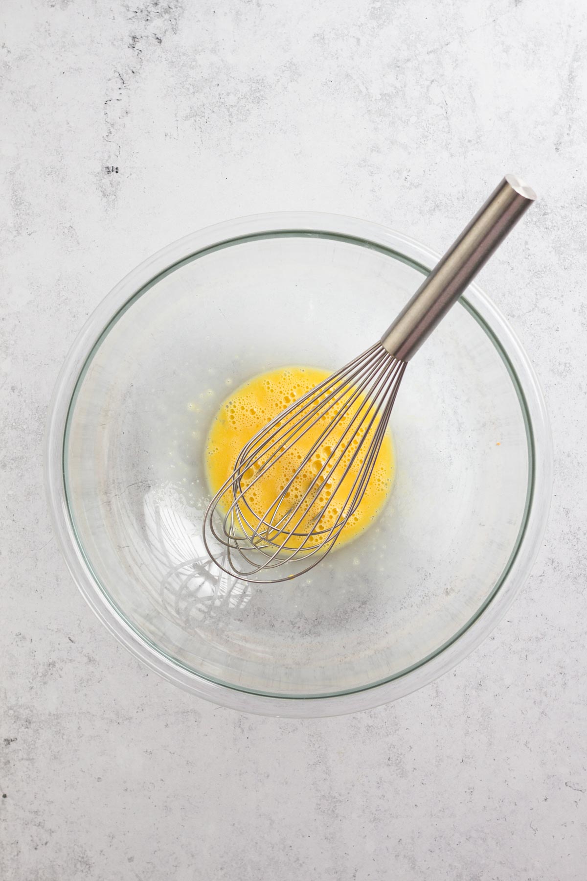overhead view of beaten egg in a glass bowl with a whisk