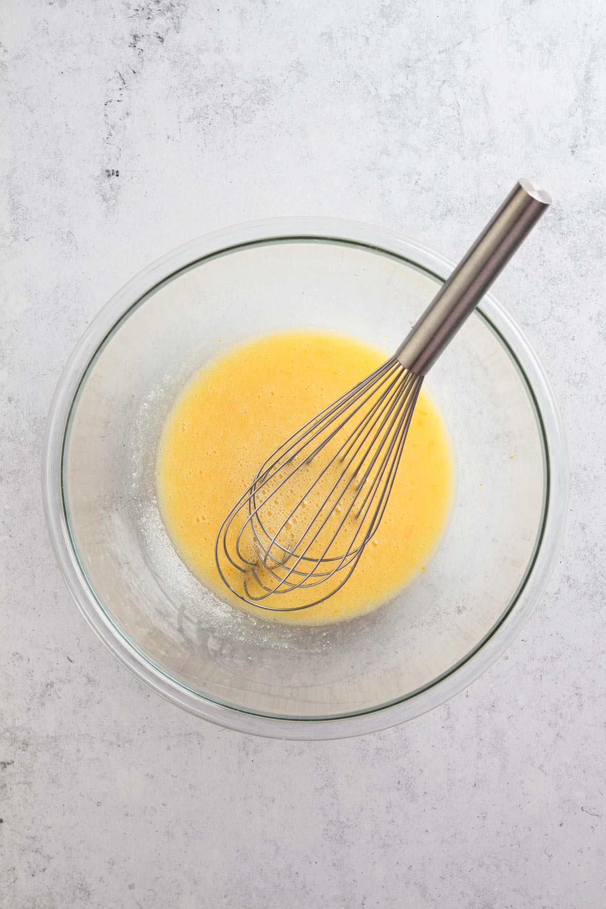 overhead view of wet ingredients in a glass bowl with a whisk