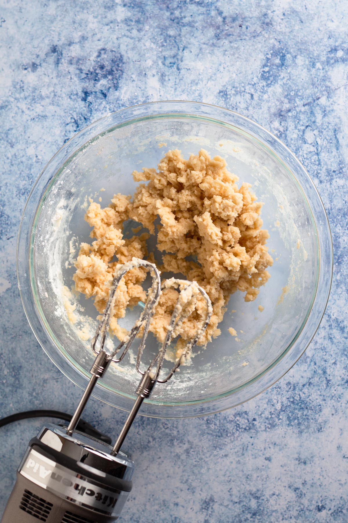 Overhead view of cookie dough in a glass bowl with a hand mixer.