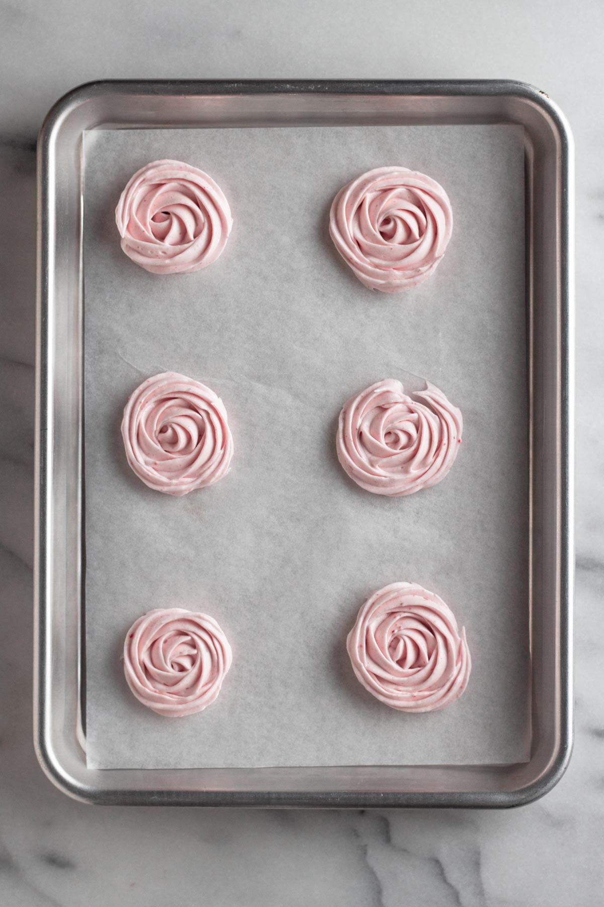 strawberry meringue piped in small rose spirals on a baking sheet