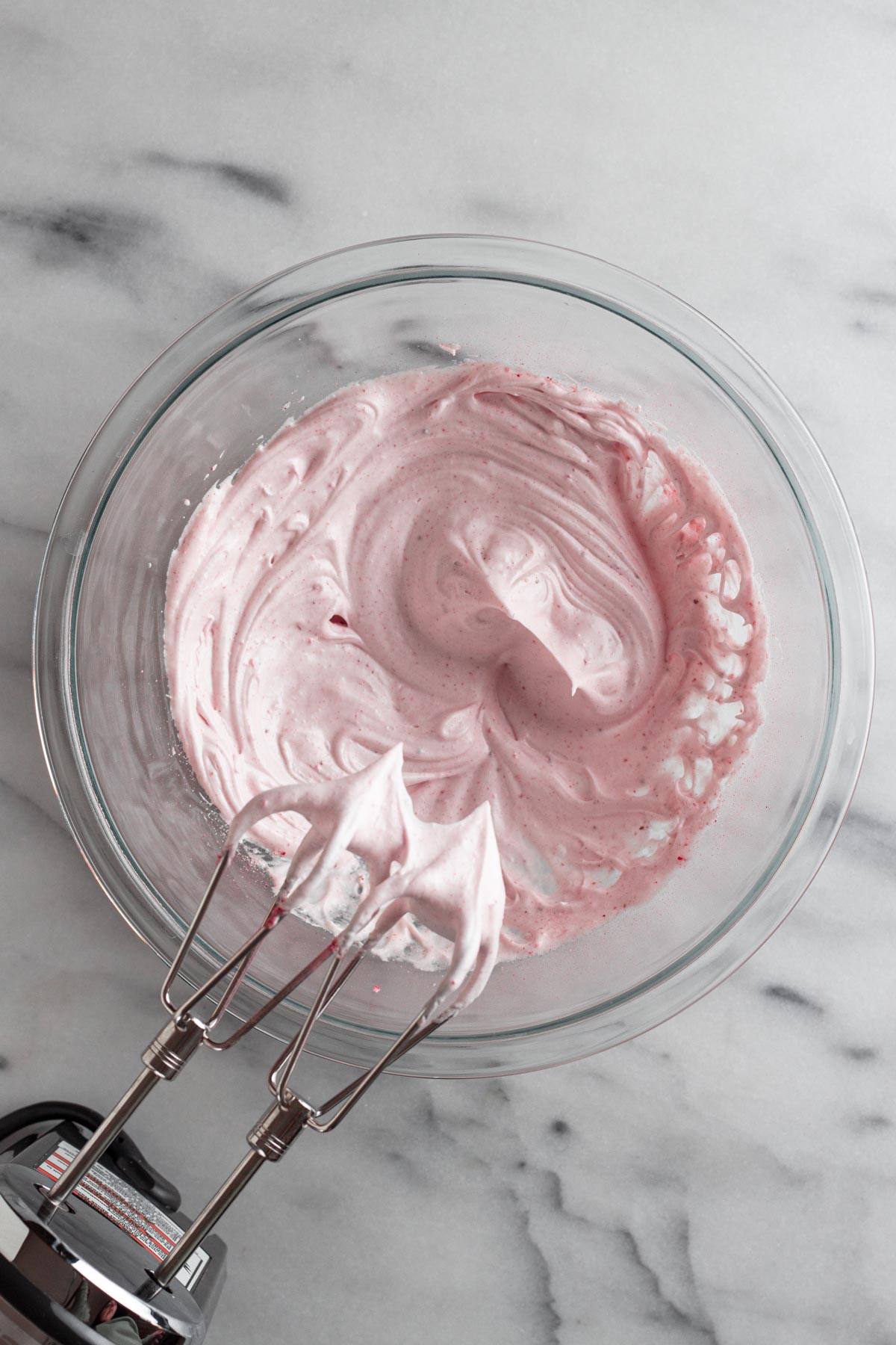 pink meringue in a glass bowl with an electric mixer