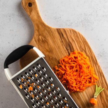 box grater and grated carrot on a wooden cutting board