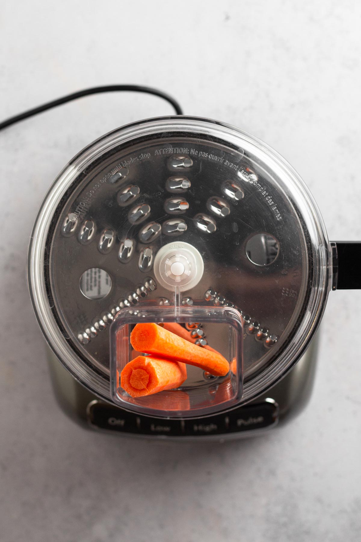 food processor with shredding disc installed and peeled carrots in feed tube