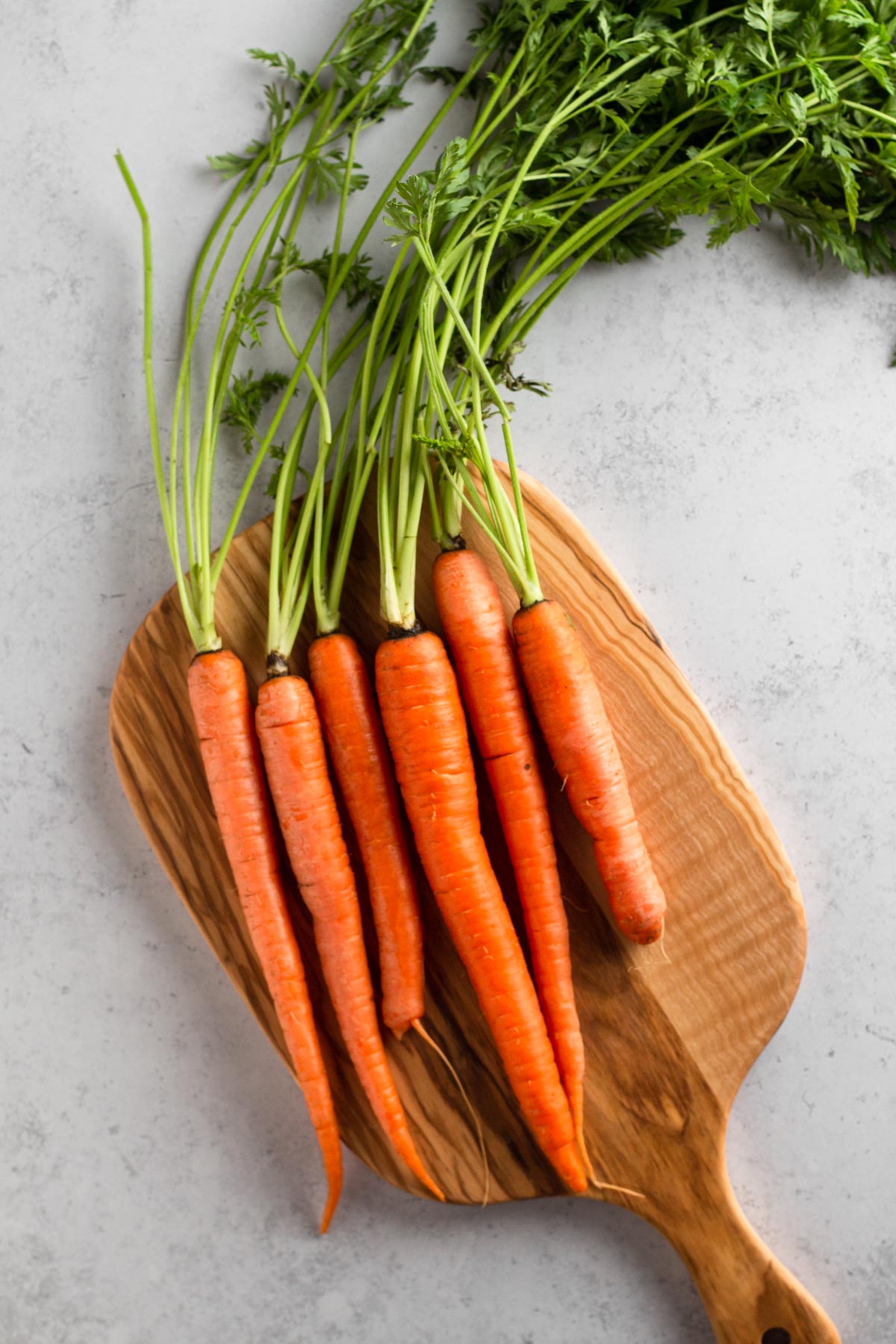 fresh carrots with stems on a wooden cutting board