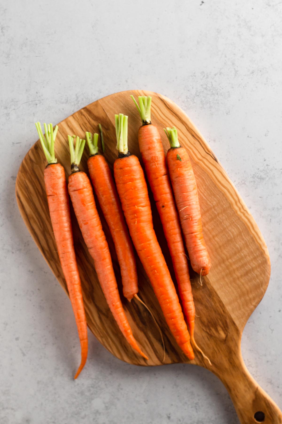 fresh carrots with stems trimmed on a wooden cutting board