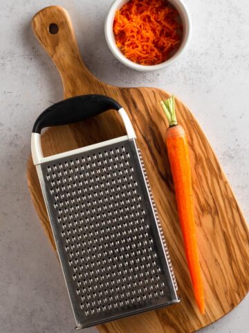 box grater and peeled carrot on a wooden cutting board