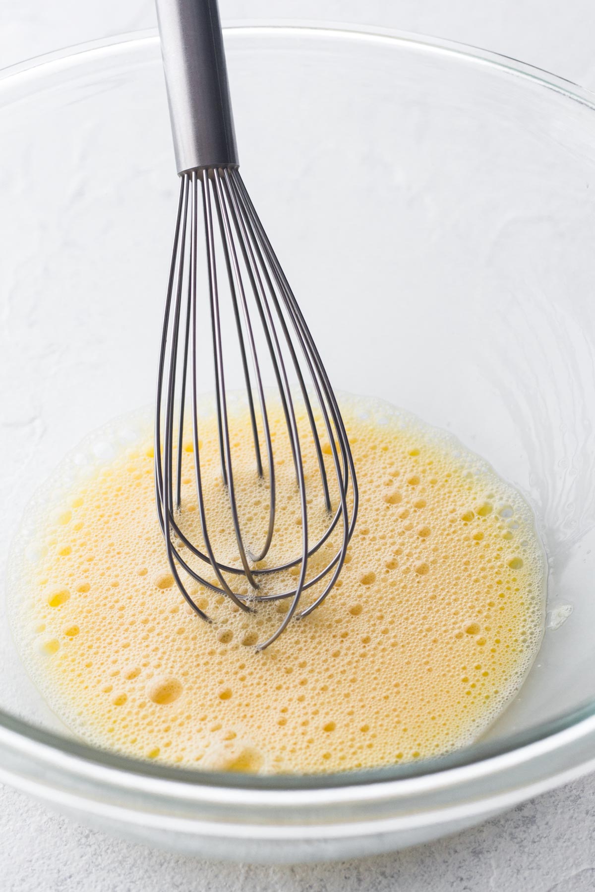 Eggs being beaten in a glass bowl with a metal whisk.