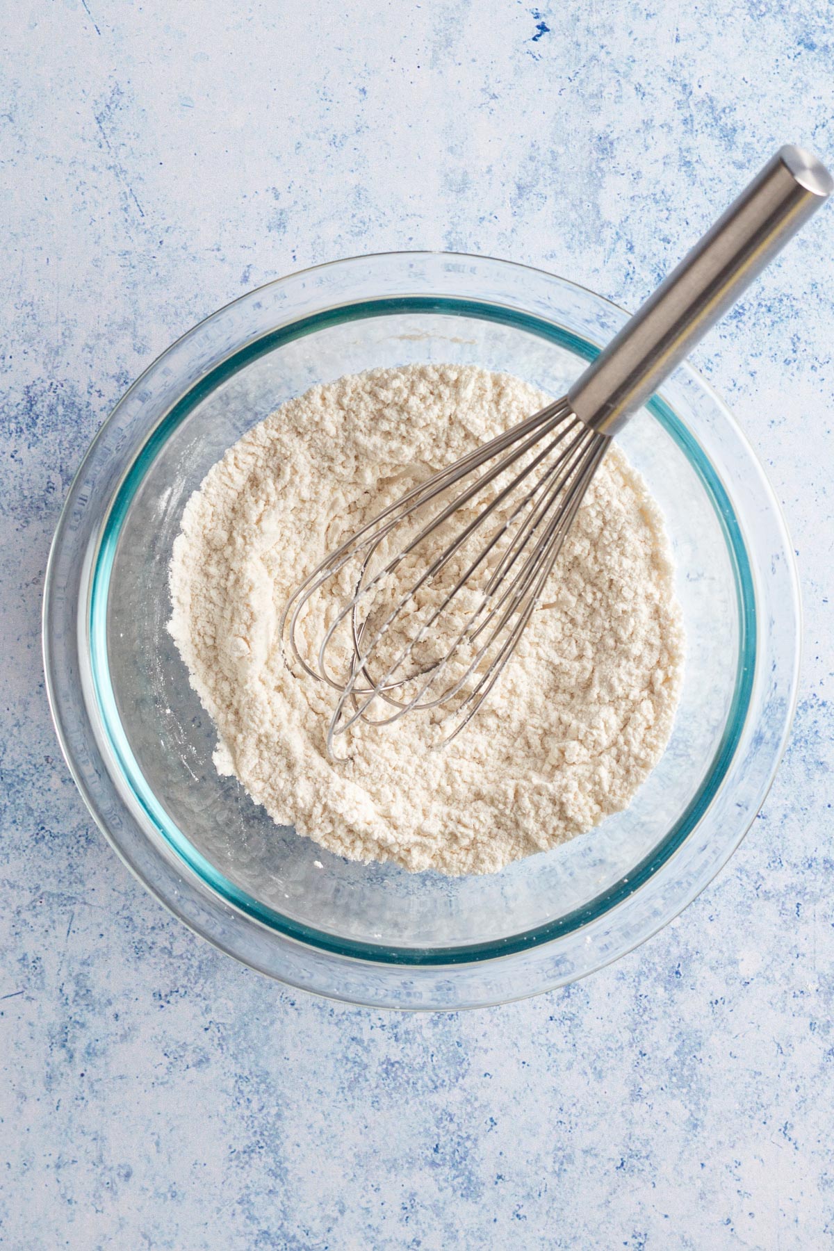 Dry ingredients in a glass bowl with a whisk.