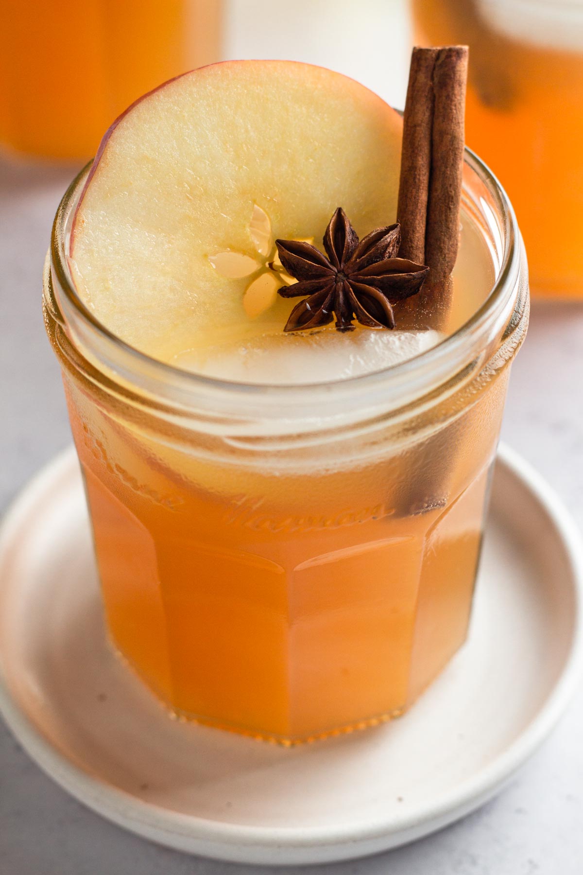 Close up view of punch in a glass on a gray surface garnished with an apple slice, cinnamon stick, and star anise.