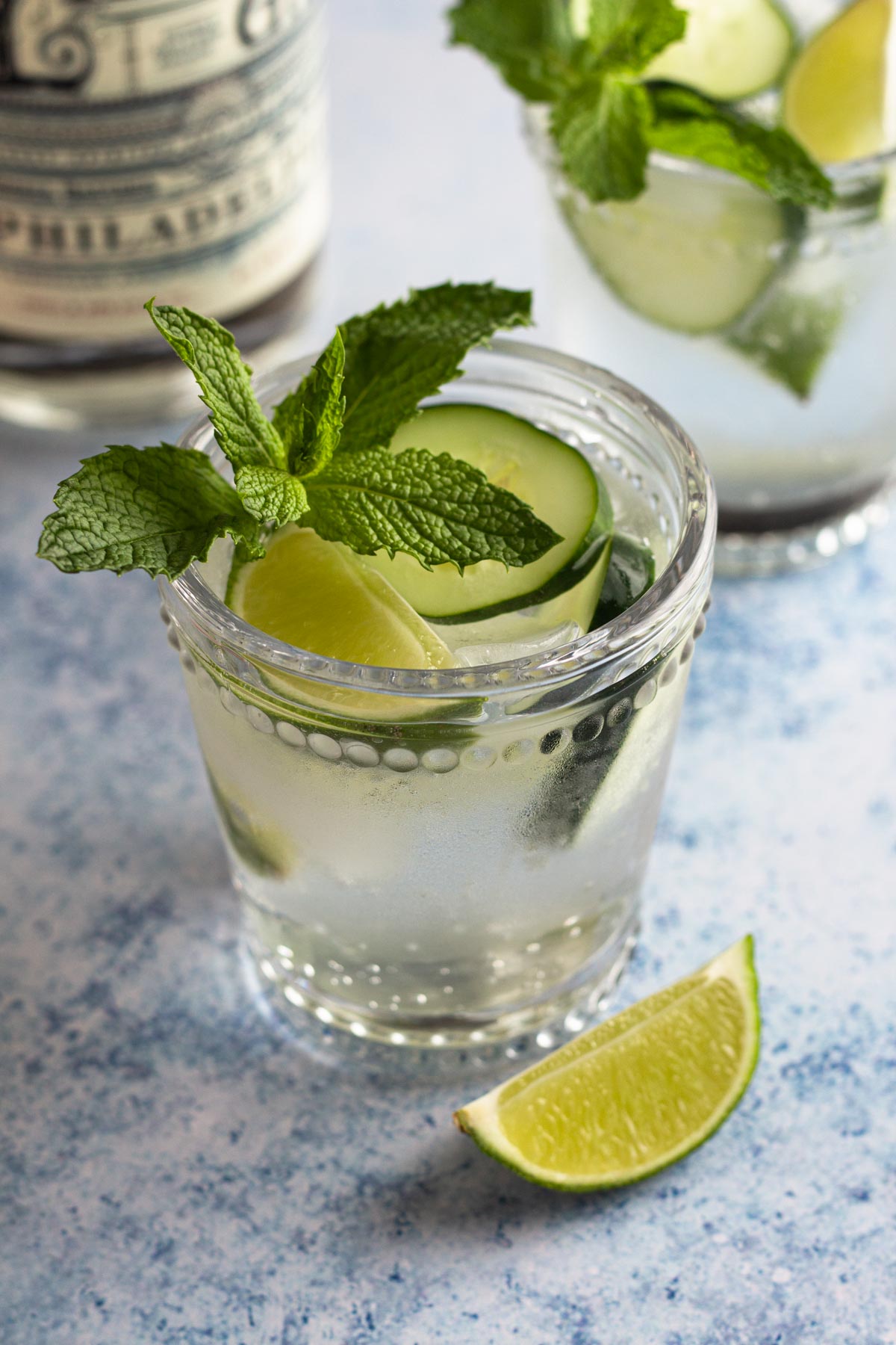 Gin and tonic garnished with a lime wedge, cucumber slices, and a sprig of mint.