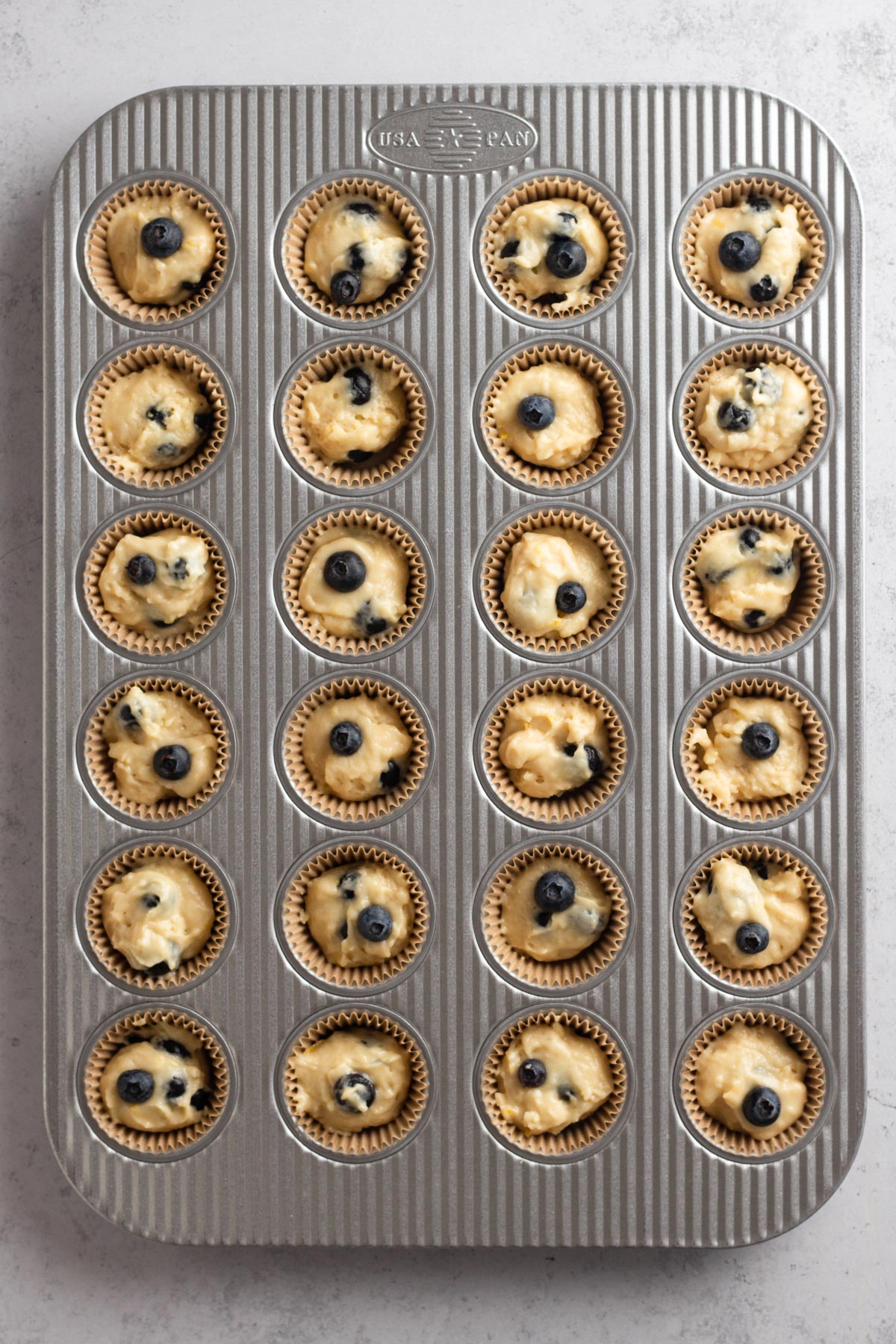 Blueberry muffins batter in paper liners in a metal muffin pan.
